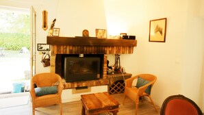 A living room with a fireplace, wicker chairs, a wooden coffee table, and a television.