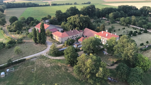 An aerial view of a large estate with multiple buildings, expansive green fields, and a well-maintained garden.