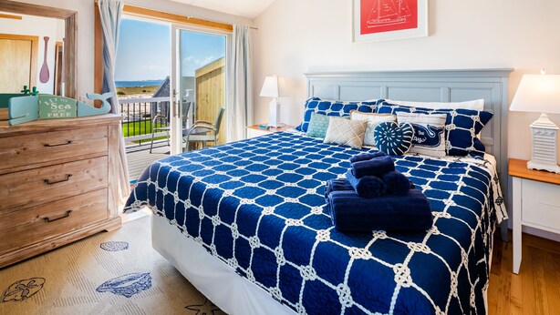 A bedroom with a large bed, wooden dresser, and a balcony with a view.