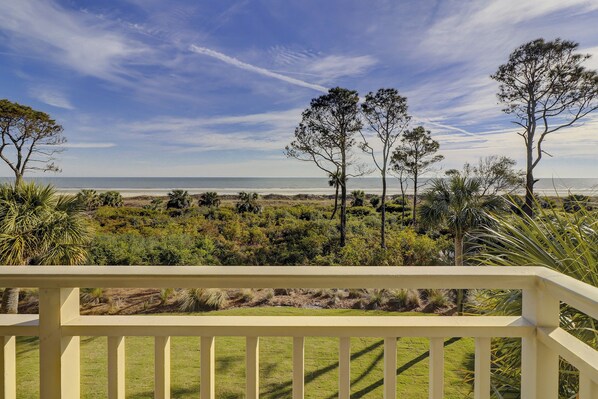A coastal landscape with a view of the ocean, a grassy area with trees, and a white railing in the foreground. - Shorewood 308 (Hilton Head Island)
