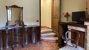 Een kamer met een houten dressoir, een spiegel, een televisie en een stoel met kussen.