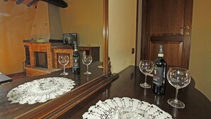 Een houten eettafel met een kantborduurwerk, wijnglazen en flessen. Achterin is een open haard zichtbaar.