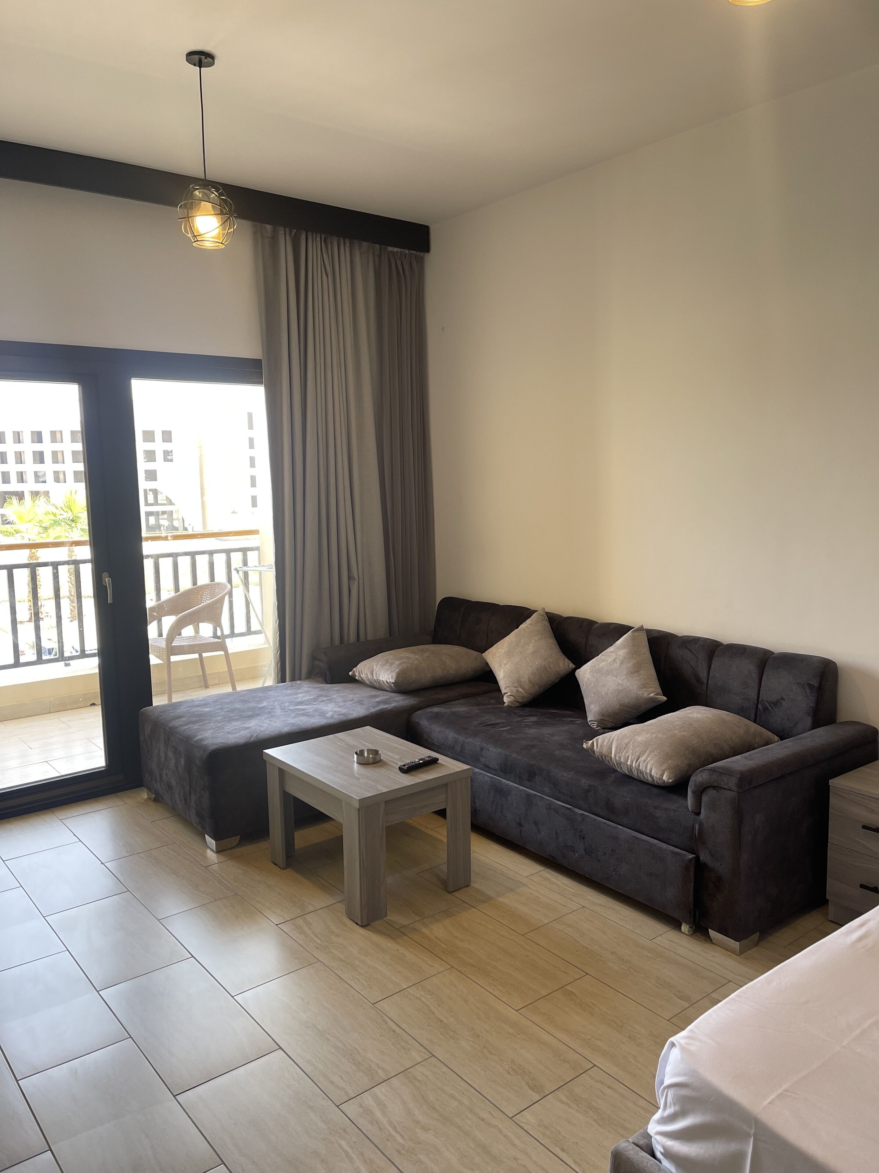 A modern living room with a grey sectional sofa, a small wooden coffee table, and a balcony with a view of buildings.
