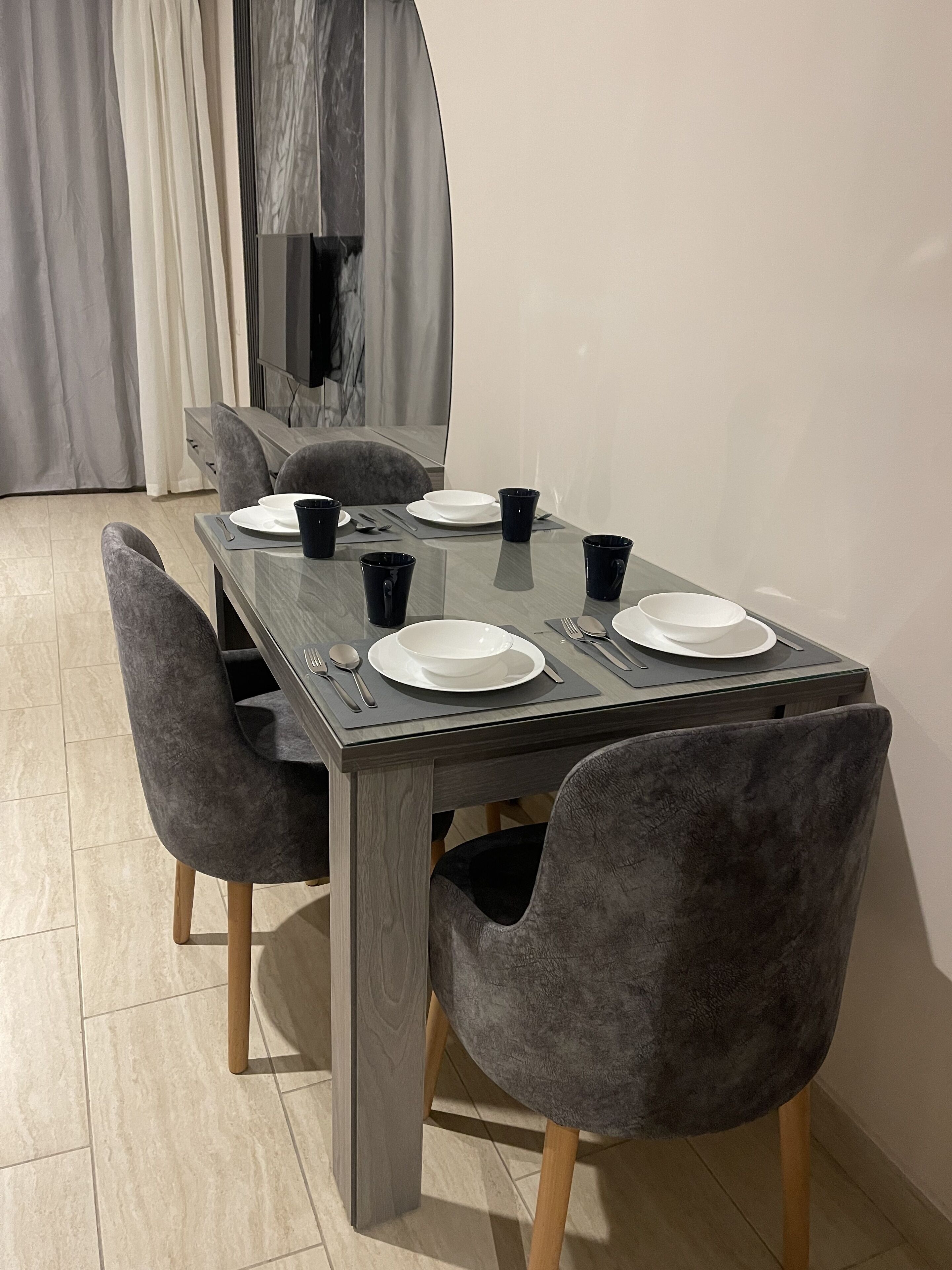 A dining table with four chairs, a flat-screen TV, and a curtain in the background.
