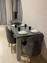A dining table with four chairs, a flat-screen TV, and a curtain in the background.