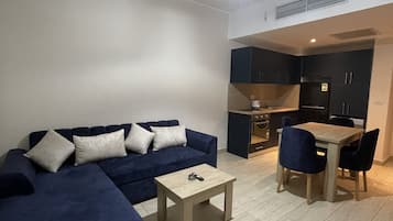 Ein modernes Wohnzimmer mit einem dunkelblauen Sofa, einem kleinen Holztisch und einem Essbereich mit zwei Stühlen.