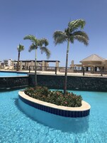 Una piscina con borde curvo, palmeras y un edificio con tejado de azulejos al fondo.