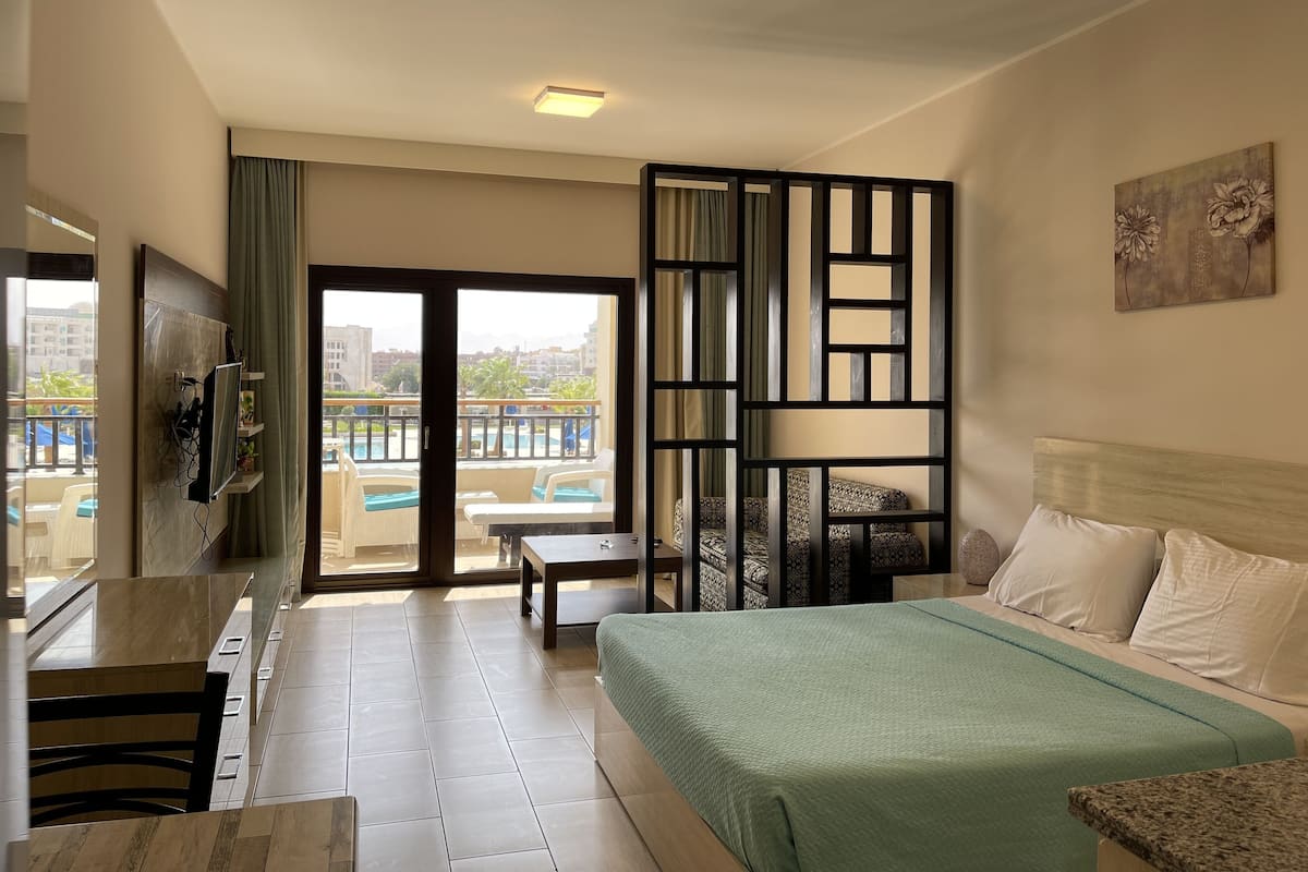 Une chambre d’hôtel équipée d’un lit, d’un bureau, d’une chaise, d’une télévision et offrant une vue sur une piscine et des bâtiments.