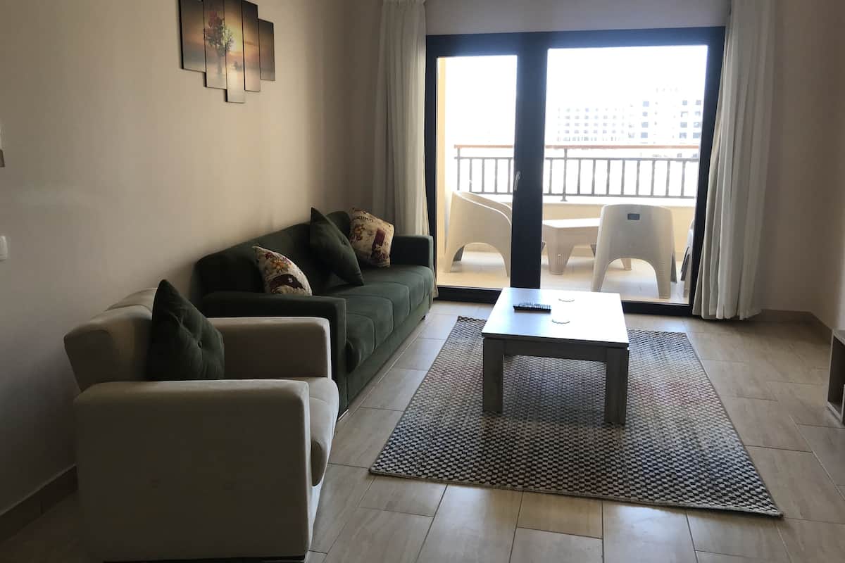Un salon comprenant un canapé, une table basse et donnant sur un balcon aménagé avec du mobilier d’extérieur.