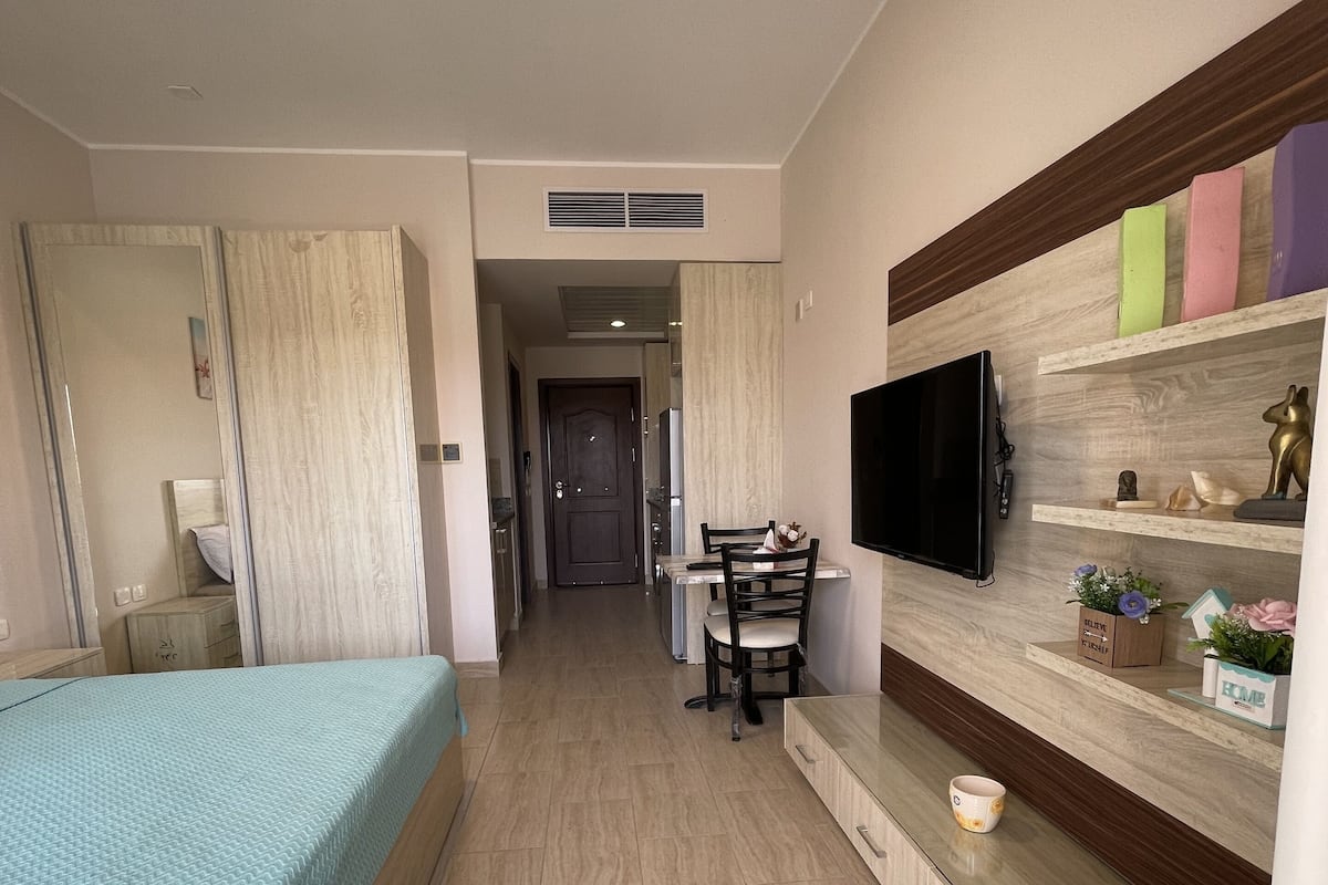 Une chambre d’hôtel équipée d’un lit, d’un bureau, d’une chaise, d’une télévision et d’une étagère où sont disposés des objets décoratifs.