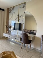 Una sala de estar moderna con un televisor montado en una pared de mármol, un sofá y un espejo grande.