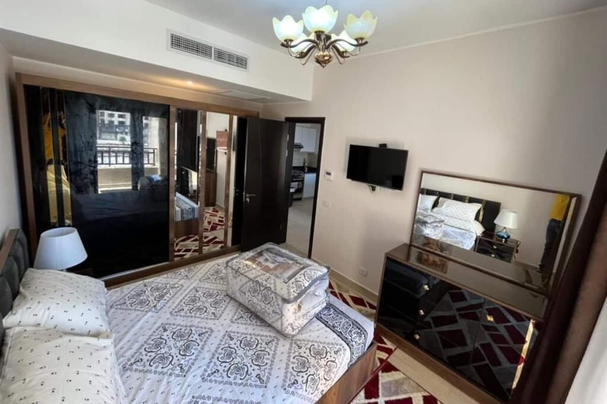 Une chambre à coucher avec un lit, une commode, un téléviseur et un grand miroir.