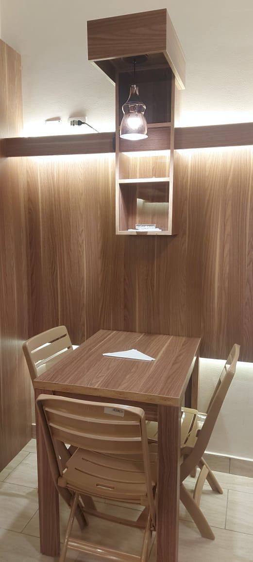 A dining area with a wooden table and chairs, a pendant light, and a built-in shelf above the table.