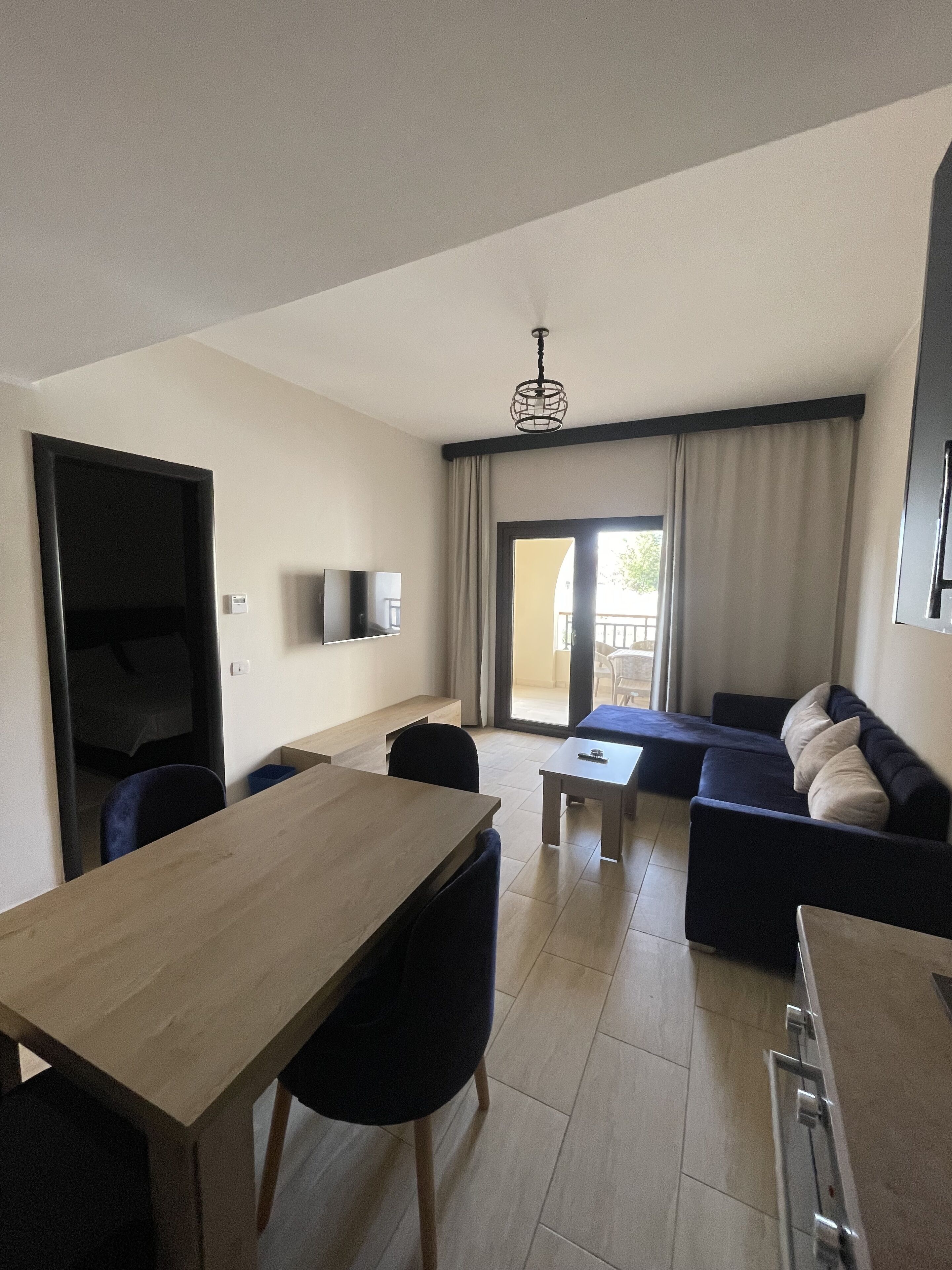 A modern living room with a wooden dining table, a sofa, and a TV mounted on the wall.