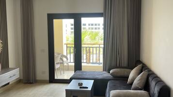 A modern living room with a sofa, a coffee table, and a view of a balcony with outdoor furniture.