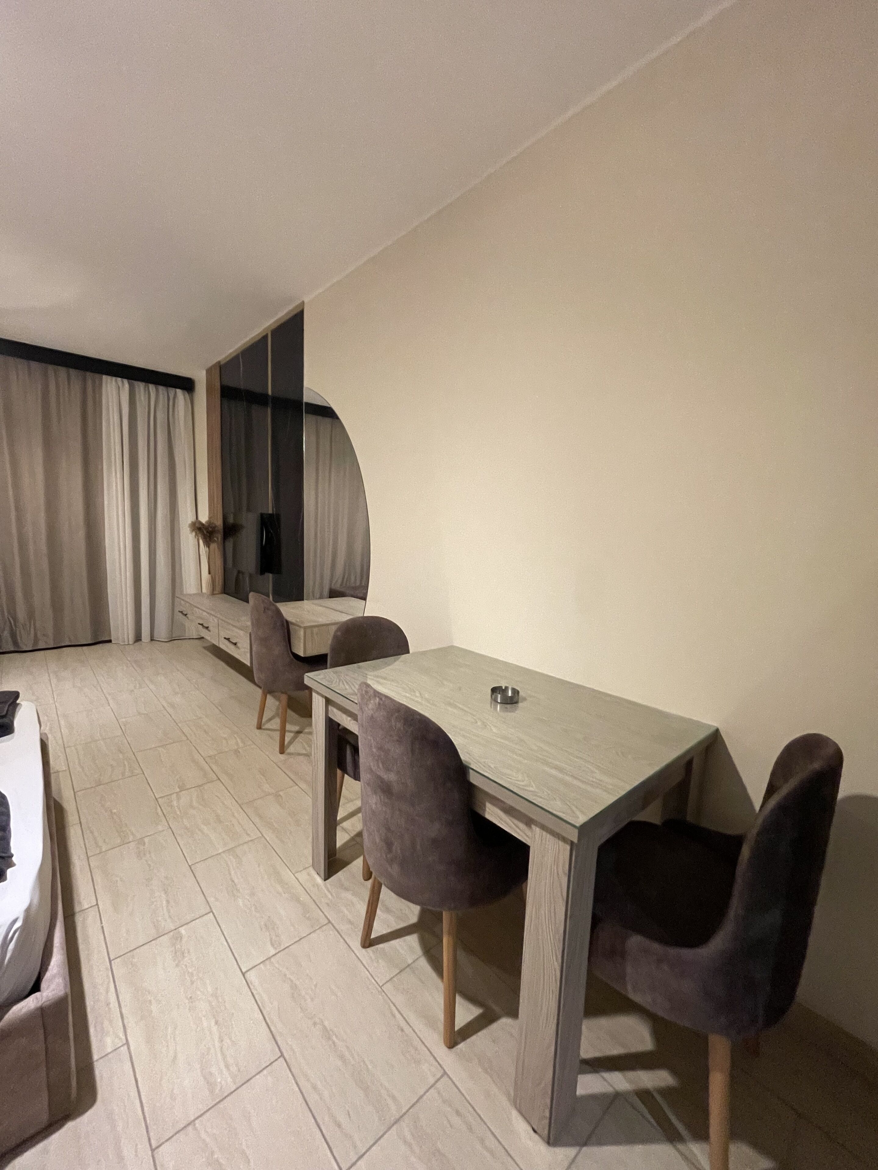 Un espace repas moderne avec une longue table et quatre chaises, un grand miroir et une vue sur l’intérieur de la pièce.