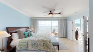 A bedroom with a bed, a ceiling fan, a view of the sea, and a balcony with chairs. - Lighthouse 2C - Beautiful Condo at The Lighthouse - Inquire Now for Specials! (Oyster Pond)