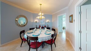 A dining room with a round table set for four, surrounded by dark wooden chairs with red cushions. A chandelier hangs from the ceiling, and a round mirror with a gold frame is on the wall. - Lighthouse 2C - Beautiful Condo at The Lighthouse - Inquire Now for Specials! (Oyster Pond)