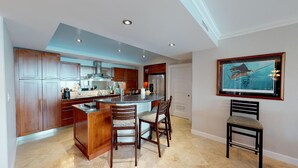 A modern kitchen with wooden cabinets, a central island, and bar stools. - Lighthouse 2C - Beautiful Condo at The Lighthouse - Inquire Now for Specials! (Oyster Pond)