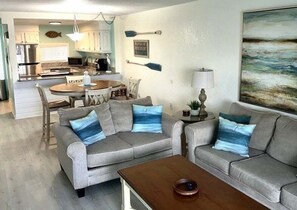 A living room with two grey sofas, a wooden coffee table, and a dining area with a round table and chairs.