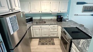A compact kitchen with white cabinets, a stainless steel refrigerator, a microwave, and a stove.