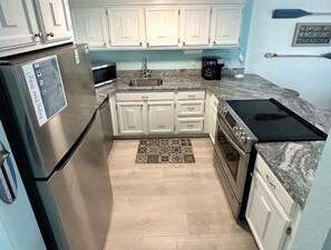 A compact kitchen with white cabinets, a stainless steel refrigerator, a microwave, and a stove.