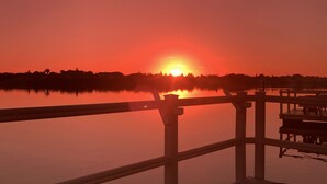 Een zonsondergang boven een kalm meer met een steiger en een leuning op de voorgrond.