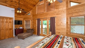 Ein Schlafzimmer in einer Blockhütte mit Bett, Sofa, Deckenventilator und einem großen Fenster.
