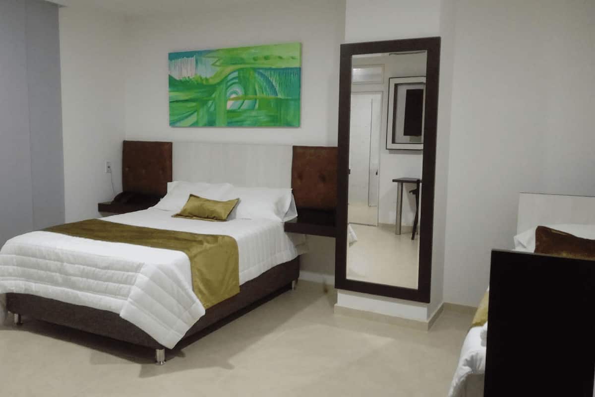 A bedroom with a bed, a nightstand, a mirror, and a painting on the wall.