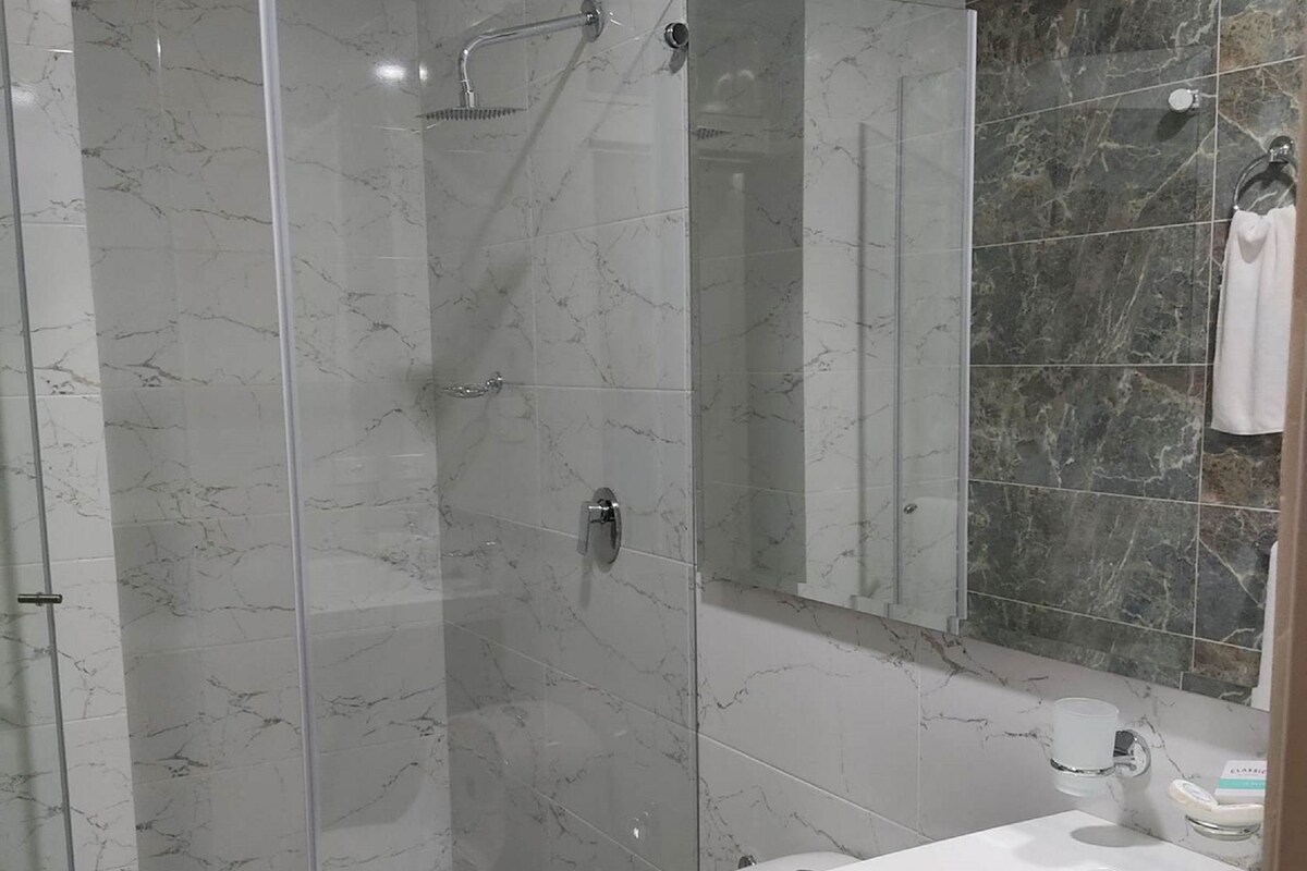 Un baño moderno con ducha envuelta en vidrio, inodoro blanco y un espejo grande sobre un lavamanos.