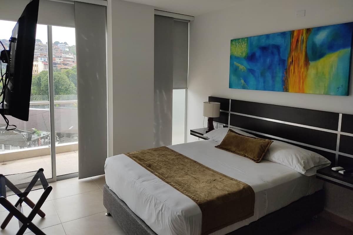 A modern hotel room with a large bed, a nightstand, a TV, and a painting on the wall.