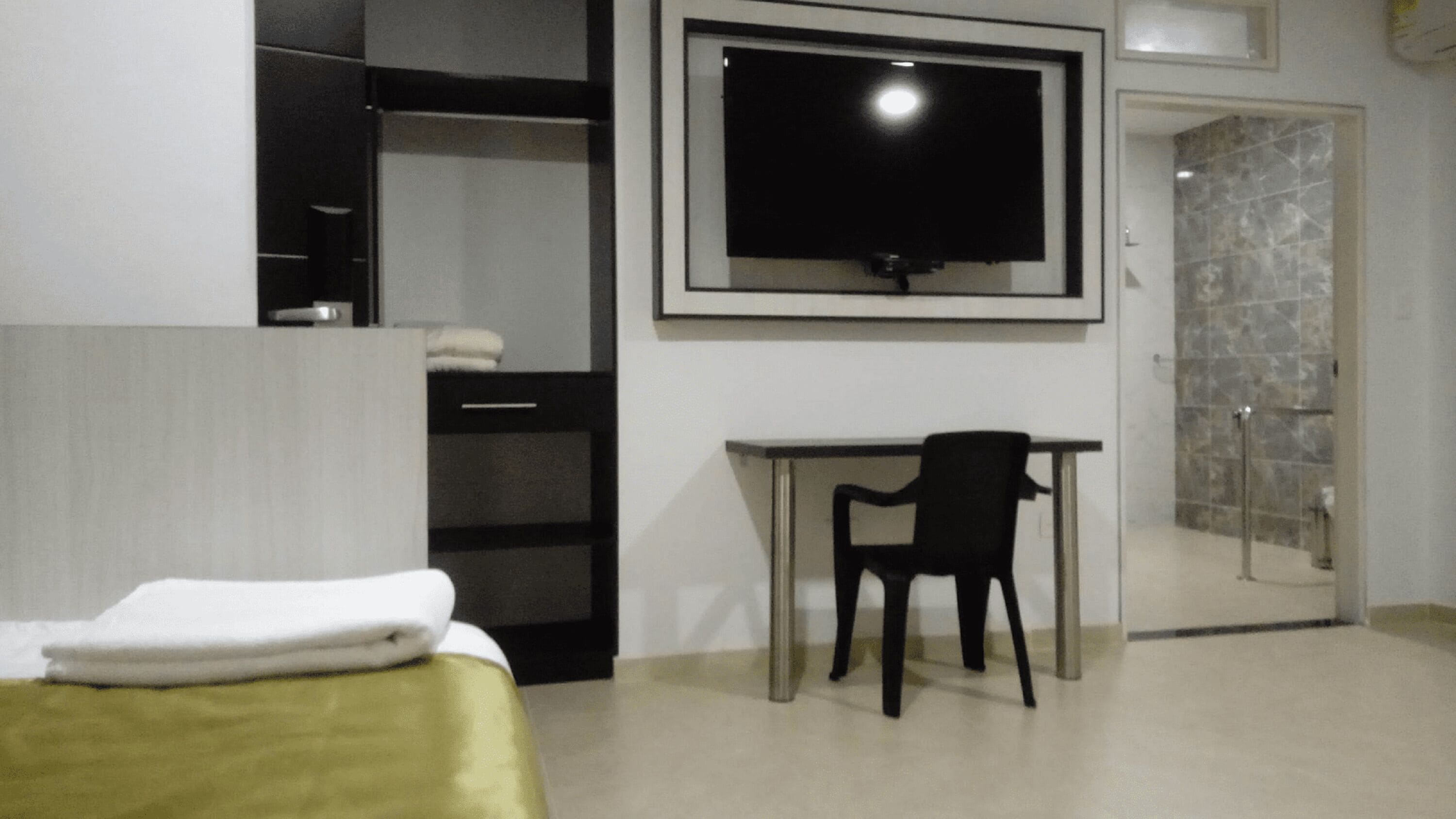 Une chambre d’hôtel équipée d’un lit, d’un bureau, d’une chaise, d’une télévision et d’une salle de bain avec une porte en verre.