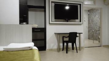 Une chambre d’hôtel équipée d’un lit, d’un bureau, d’une chaise, d’une télévision et d’une salle de bain avec une porte en verre.