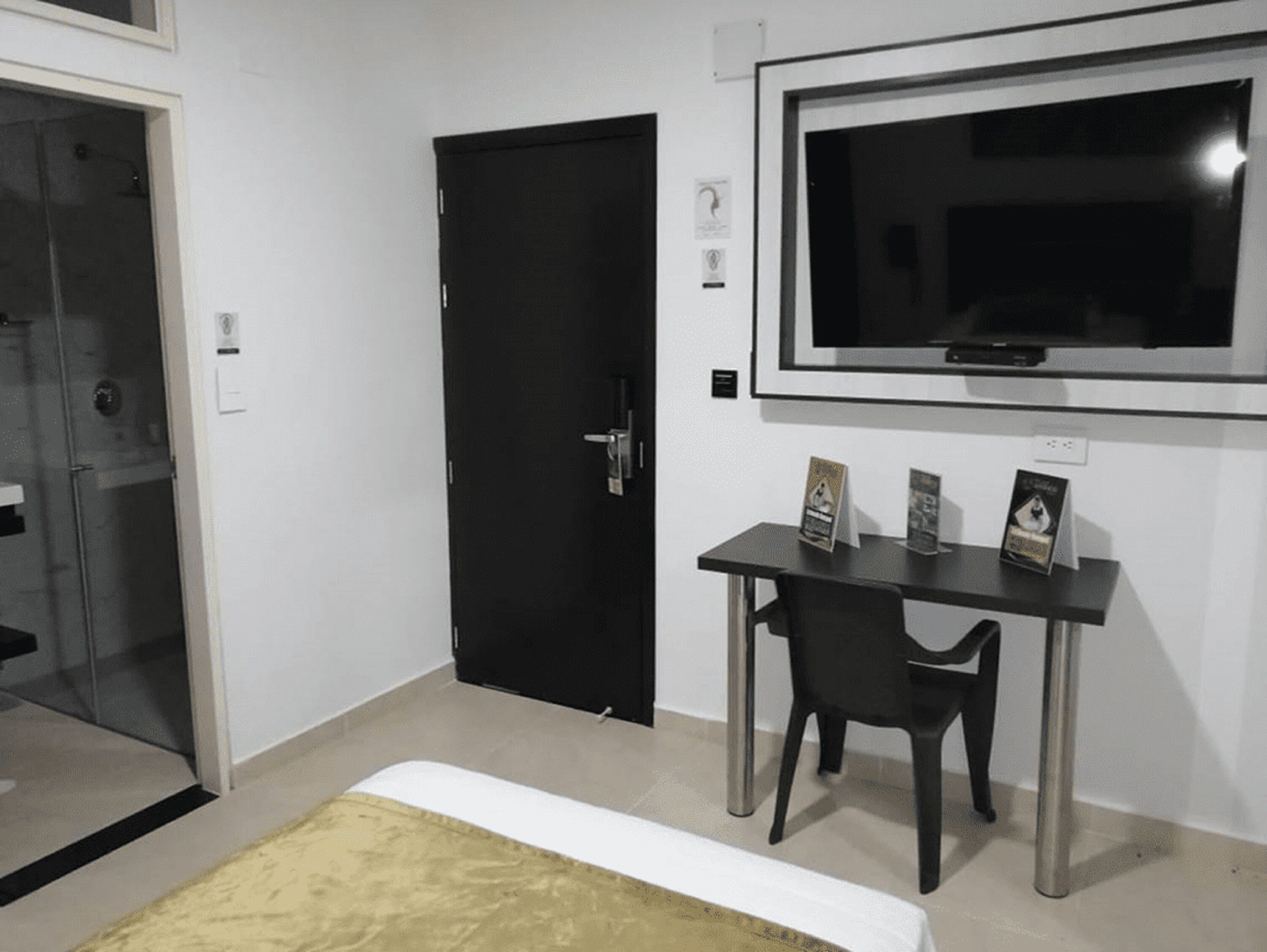 A room with a black door, a TV mounted on the wall, and a small table with chairs.