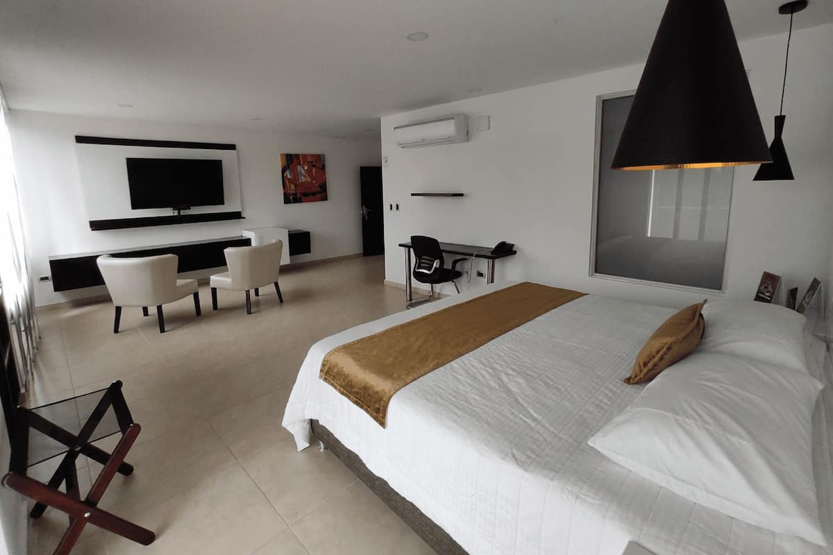 A modern hotel room with a large bed, a desk, a chair, a TV, and a large window.
