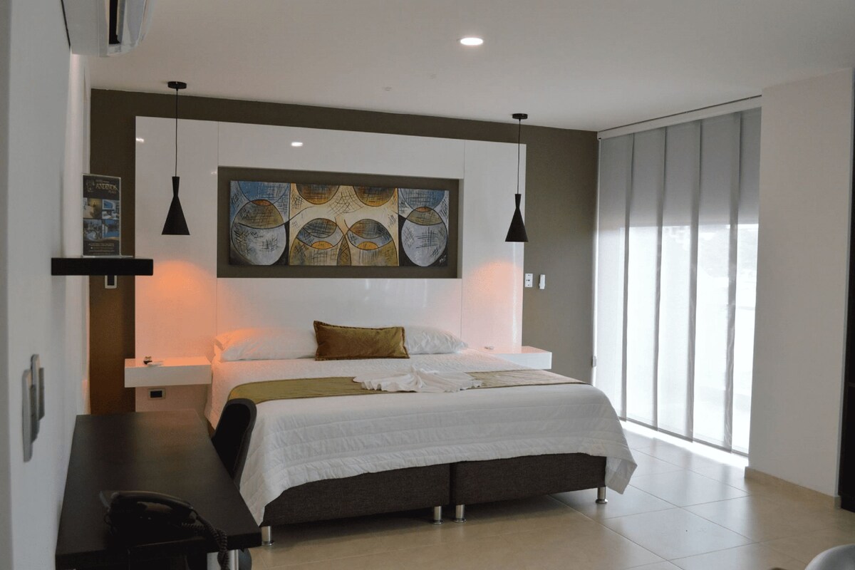 Una habitación de hotel moderna con una cama grande, un escritorio y un amplio ventanal.