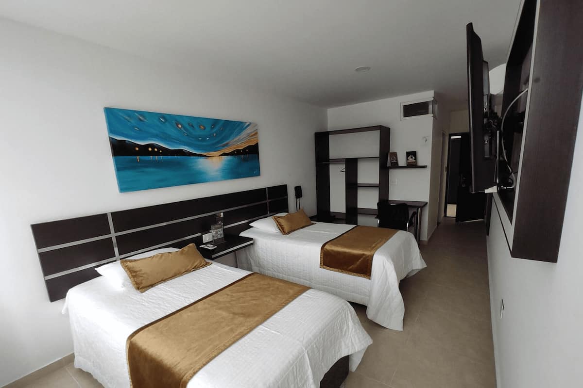 A hotel room with two beds, a painting on the wall, a desk, and a TV.