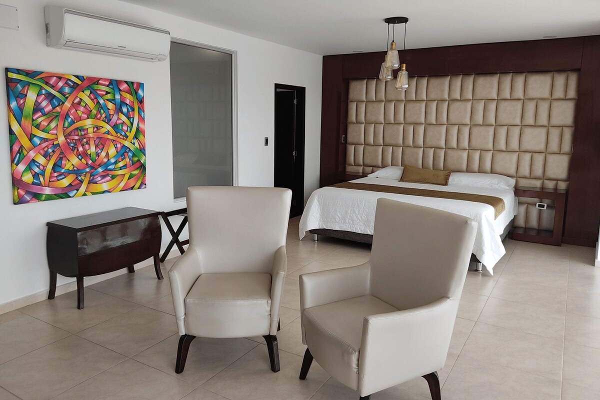 Una habitación de hotel moderna con una cama grande, un cabecero con diseño capitonado, un escritorio y un cuadro abstracto y colorido en la pared.