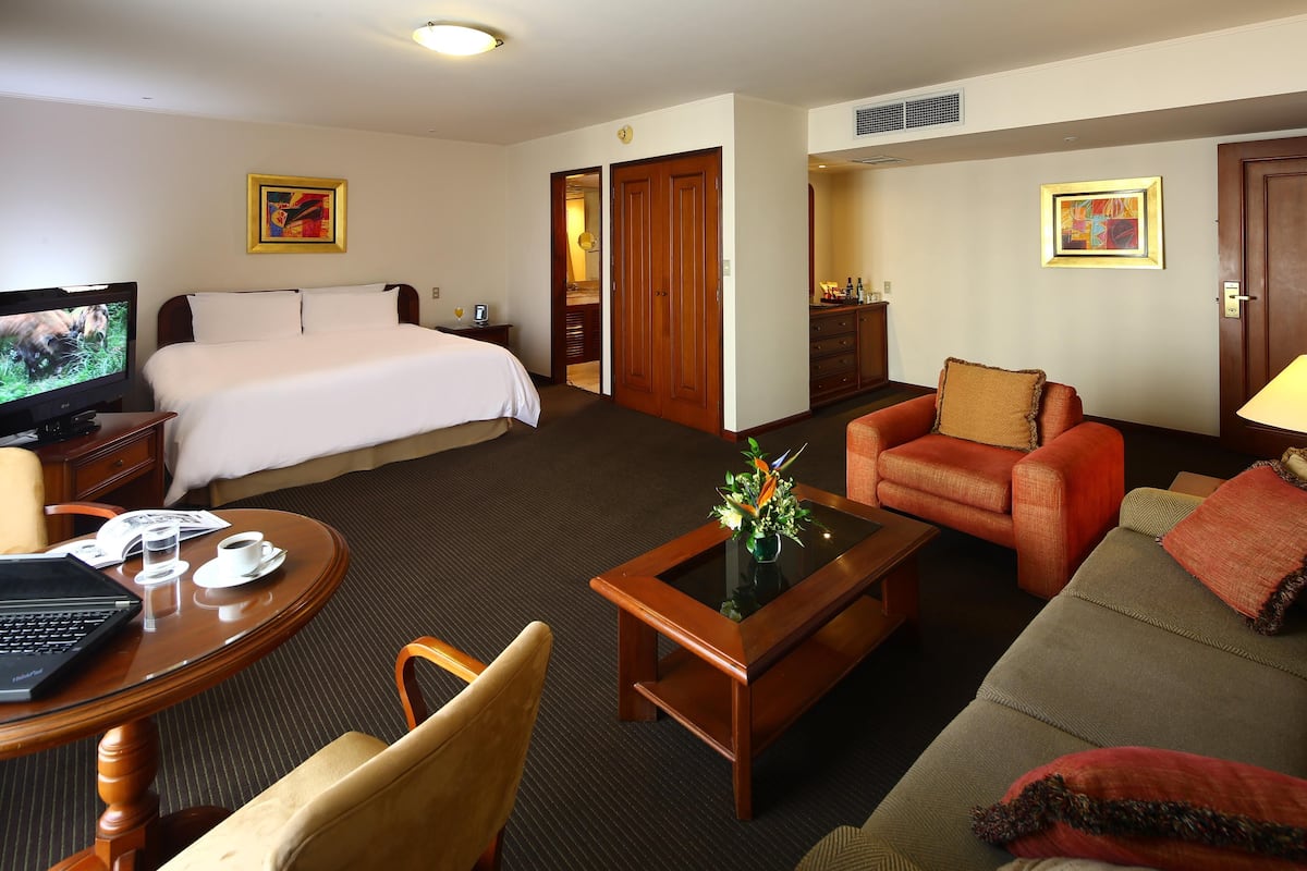 Habitación de hotel con cama, sofá, mesa de centro, televisor y escritorio con una computadora portátil.