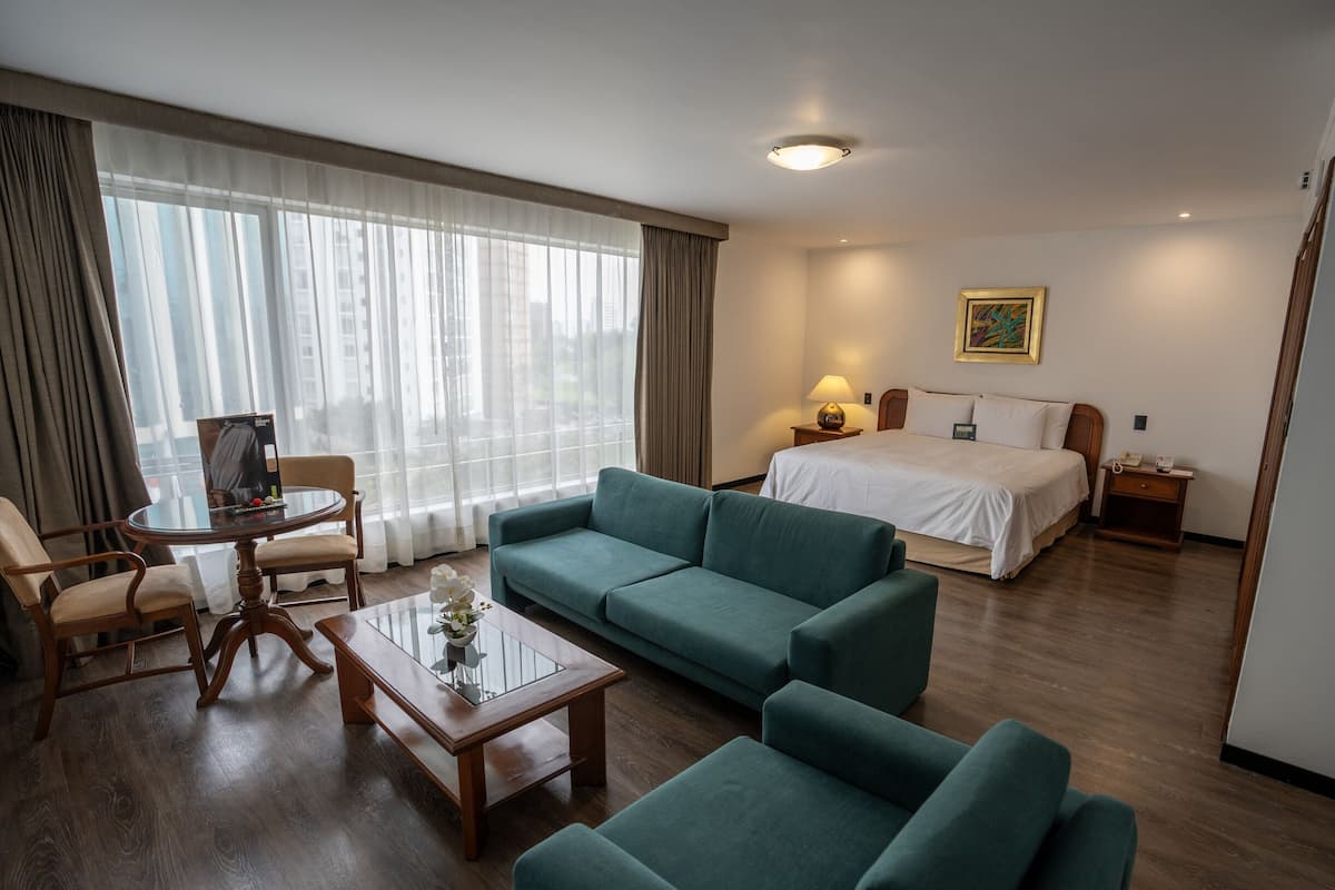 Una habitación de hotel con una cama, un sofá verde, una mesa de centro de madera y una silla.