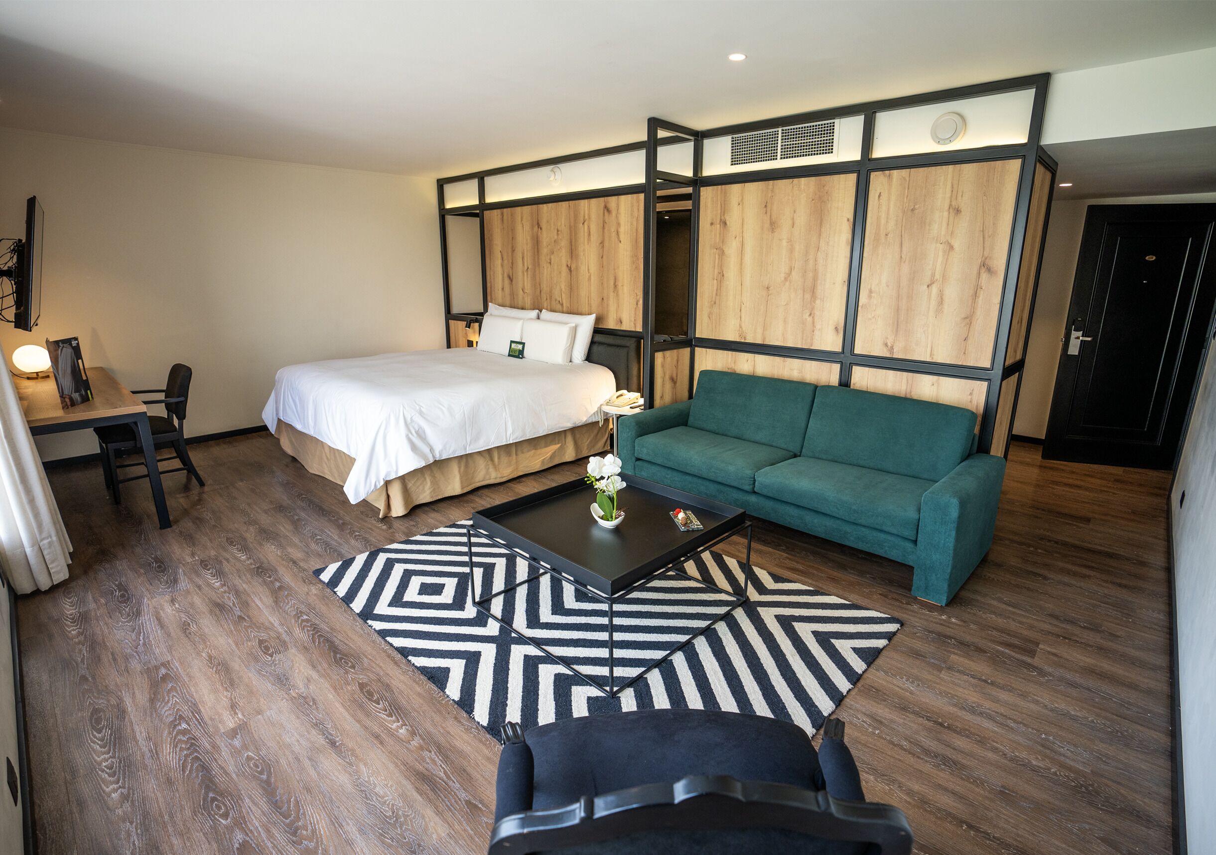 Una habitación de hotel moderna con una cama, un sofá verde, una mesa de centro negra y un escritorio con una silla.