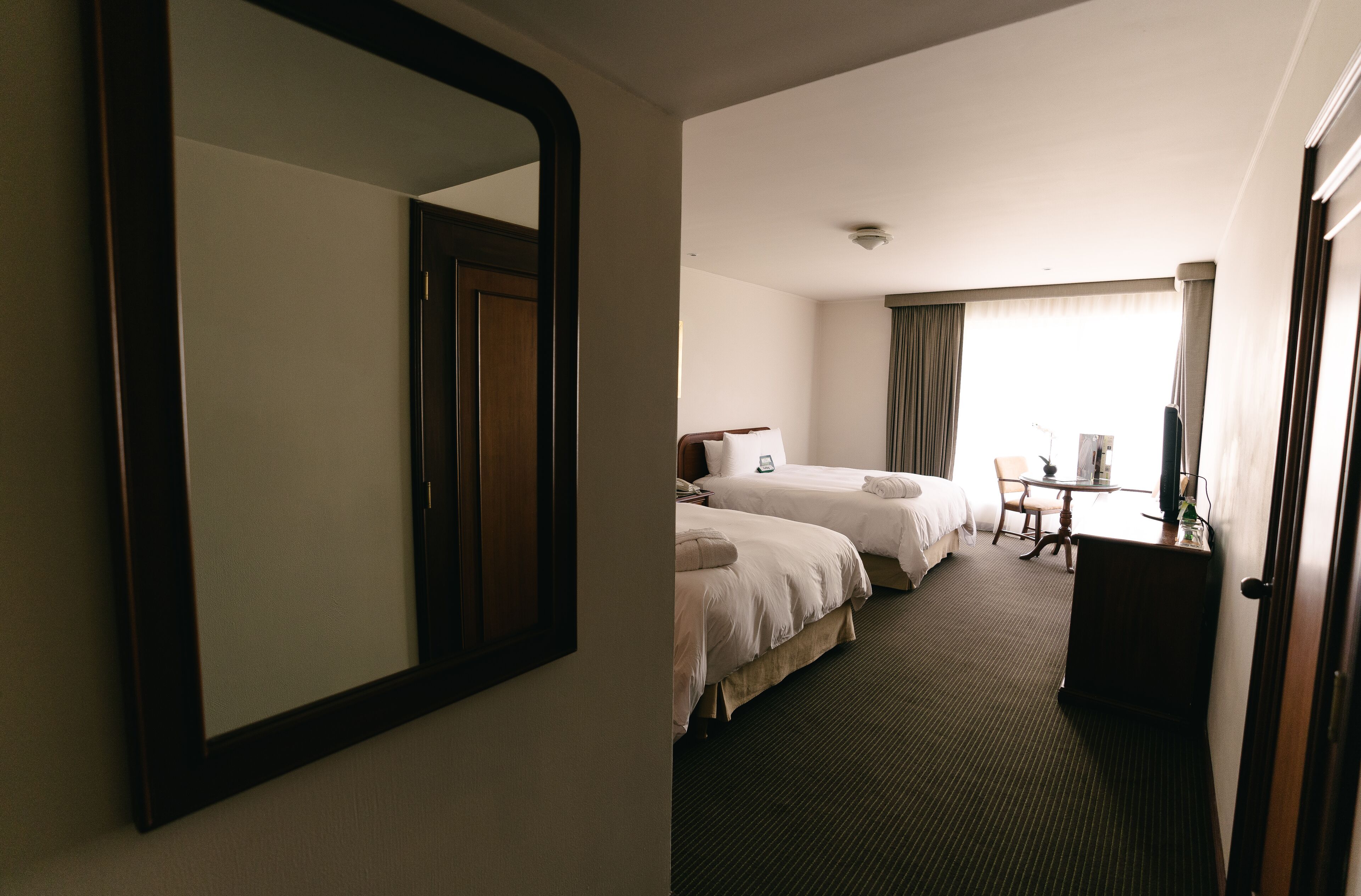 A hotel room with two beds, a desk, a chair, and a large mirror.