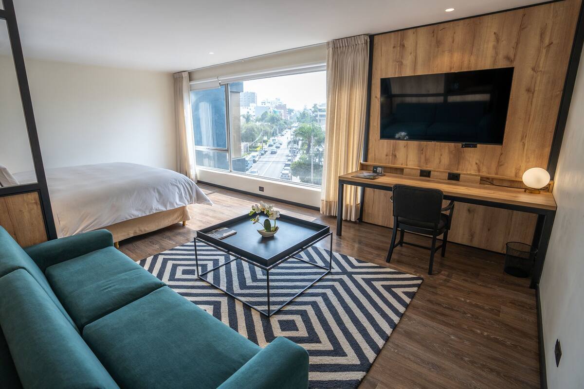 Habitación de hotel moderna con cama, sofá, escritorio, televisión y vista de la ciudad.
