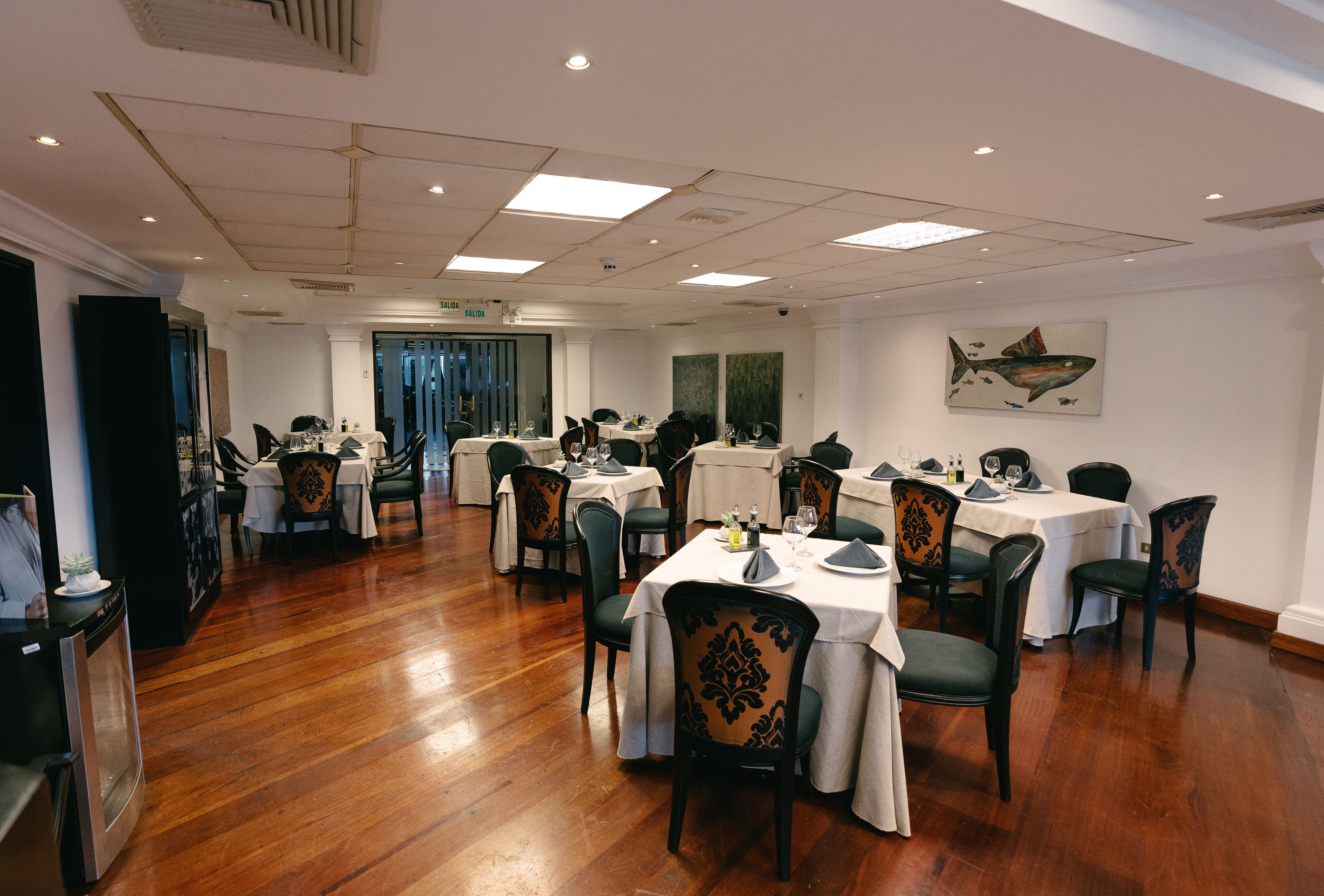 A dining area with multiple tables and chairs, wooden flooring, and a ceiling with recessed lighting.