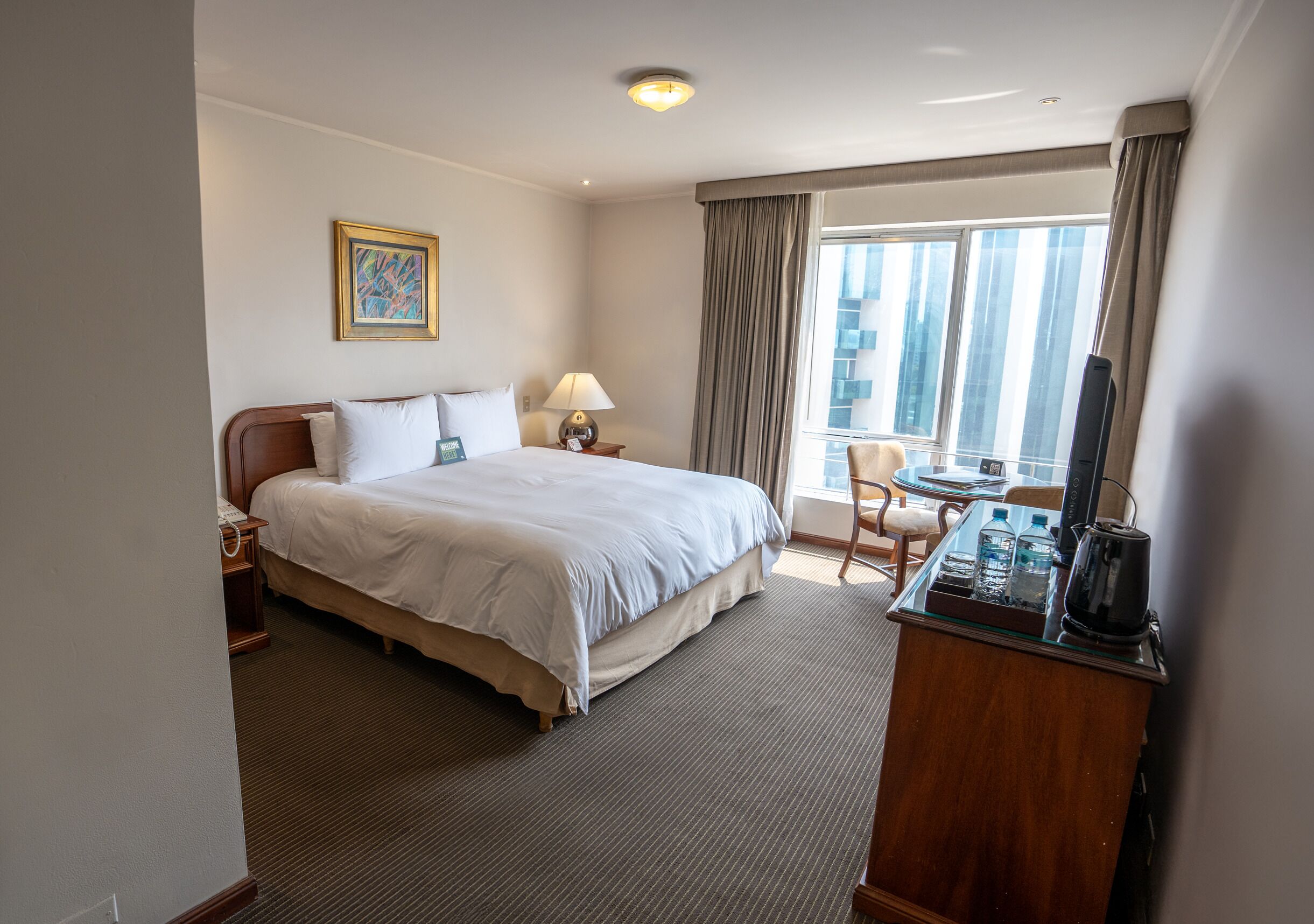 Une chambre d’hôtel avec un grand lit, un bureau avec une bouilloire, une chaise et une fenêtre avec des rideaux.