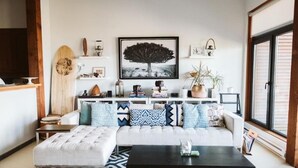 Un soggiorno moderno con un divano bianco, cuscini decorati, un tavolino da caffè nero e un'ampia finestra.