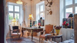 A cozy room with a rustic wooden ceiling, a large window with curtains, a chandelier, a table with a lamp, and a chair. - Lovely home in Klippan with sauna (Klippan)