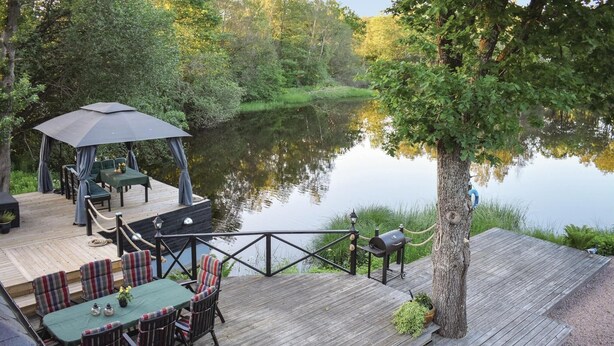 A wooden deck with a table and chairs, a gazebo, and a view of a calm lake surrounded by trees. - Lovely home in Klippan with sauna (Klippan)
