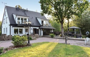 A two-story building with a stone foundation, a balcony, and a covered outdoor seating area with tables and chairs. - Lovely home in Klippan with sauna (Klippan)