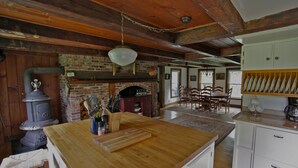 A rustic kitchen with a wooden island, brick fireplace, and a dining area with wooden chairs. - Vermont Farmhouse in the Heart of the Green Mountains (Granville)